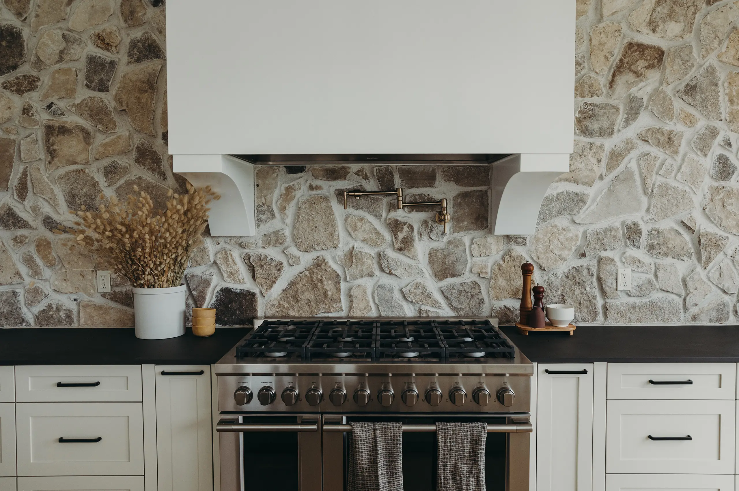 Custom kitchen design for 2022 Talbotville Dream Home by Woodfield Design + Build featuring stone backsplash, gas range, and custom cabinetry.
